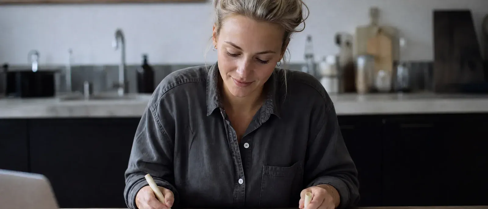 The founder of a small skincare brand highlights matching rows on two printouts at her kitchen table, comparing store orders with a report.