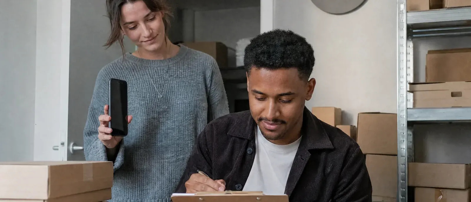 On the evening before Black Friday, the owner of an online gift shop ticks the last item on a printed checklist in a warehouse office full of parcels.