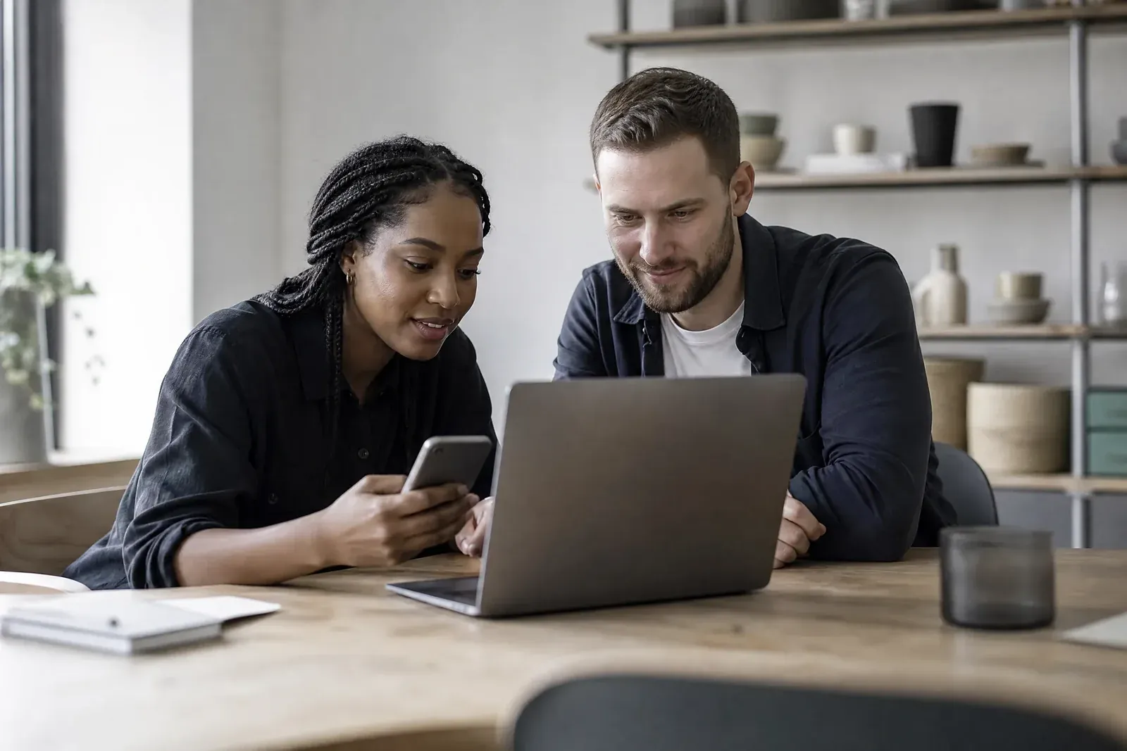 Two people at a desk test a website: one submits a test form on a phone while the other watches a debugging view on a laptop.