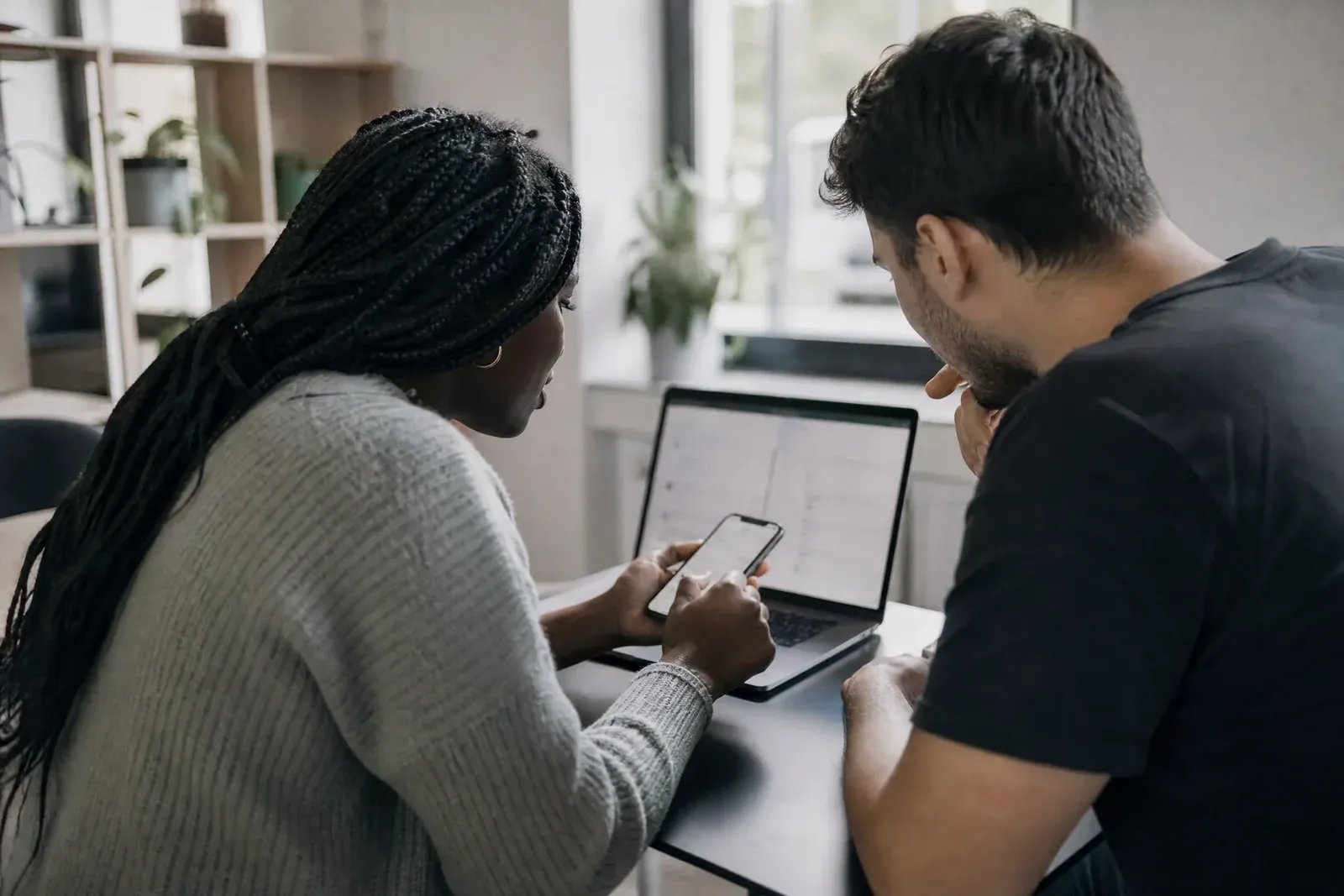 Two people at a desk test a website: one submits a test order on a phone while the other watches a debugging view on a laptop.