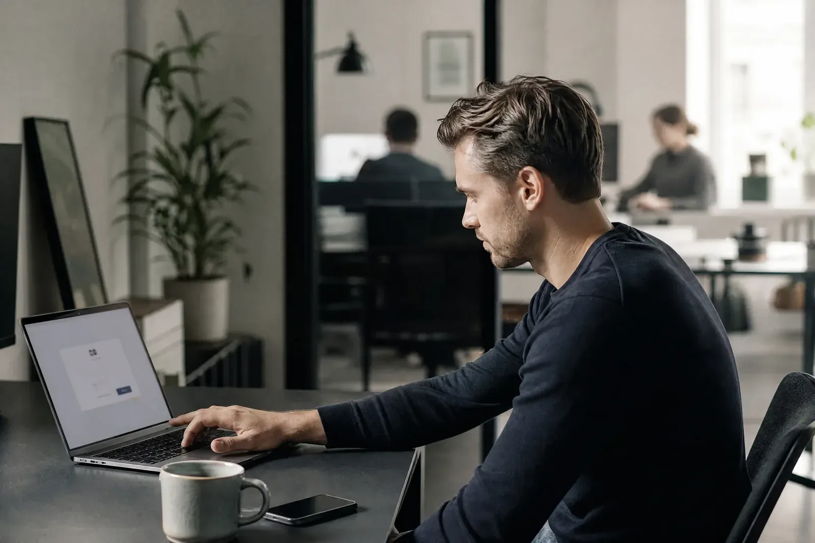 A marketer at a desk is about to click an approval button on a laptop sign-in screen.