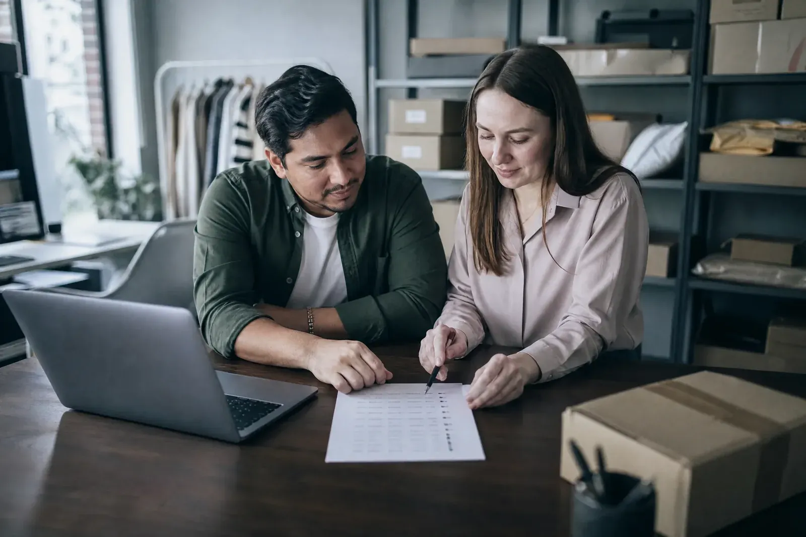 An owner and a marketer at a table with a laptop and a ticked list, planning which accounts to connect.