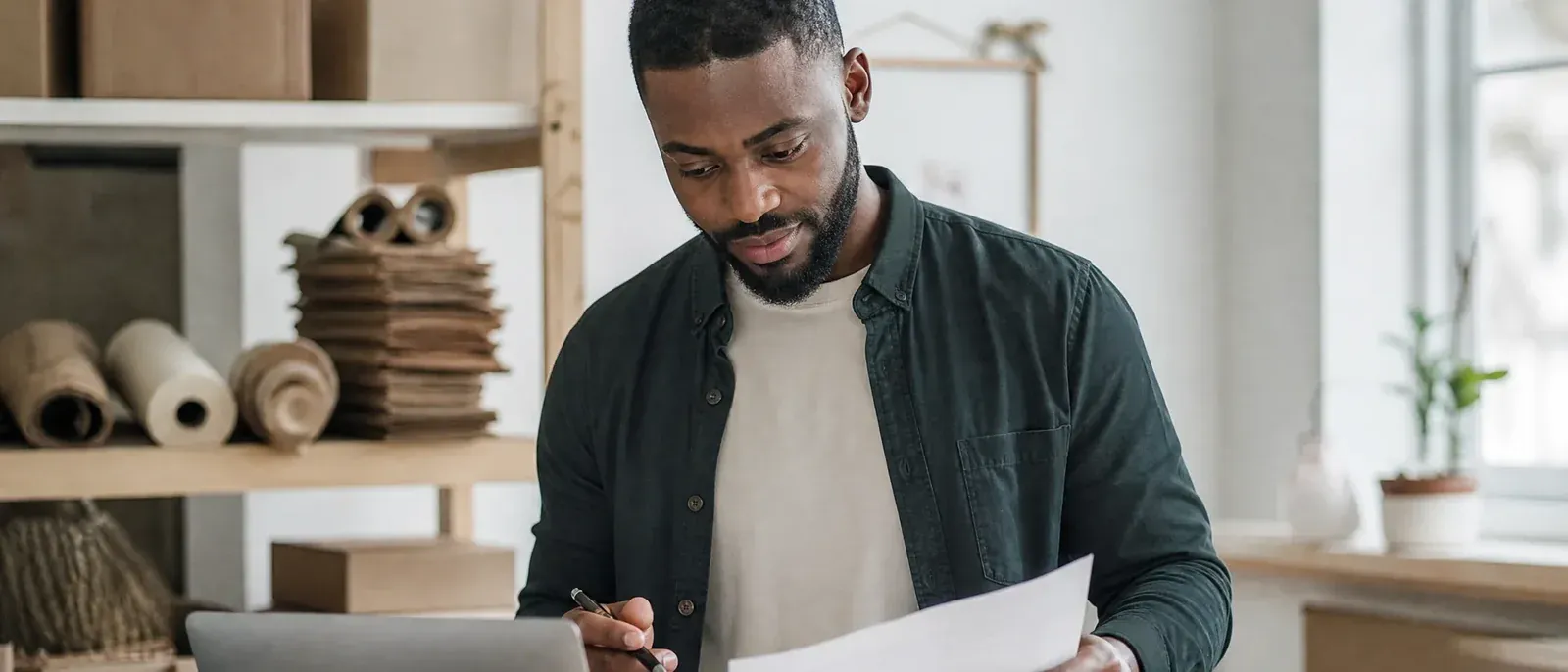 In the packing room of a small online homeware shop, the marketing lead holds a printed report next to his laptop and checks its lines against the shop's order list.